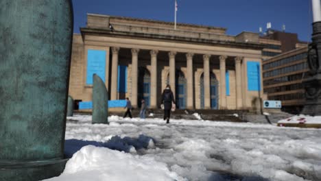 Woman-walking-in-snow-outside-city-hall-on-sunny-day,-Sheffield,-low-angle