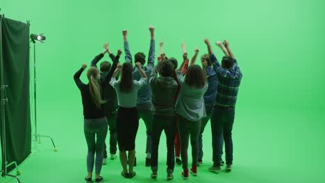 green screen chroma key studio: two rows of nine diverse fans cheering, jumping, applauding with hands in the air at the public sport event, concert, festival, party. back view full shot. slow motion