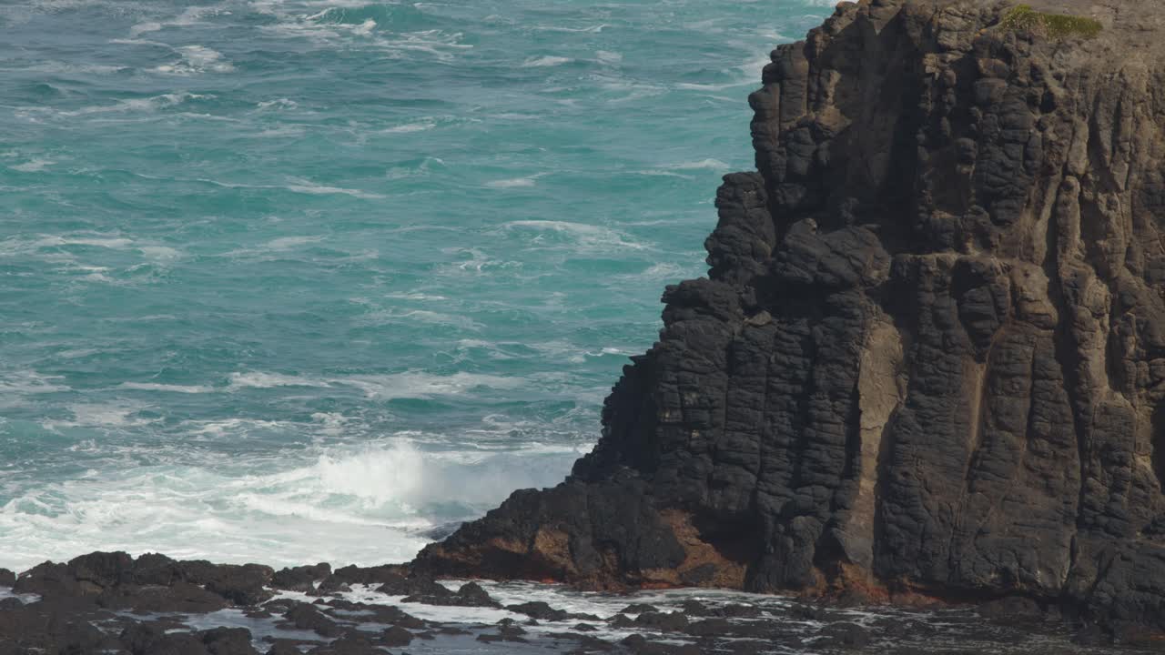 Steep basalt cliffs and turquoise ocean waves under daylight, static camera, natural coastal landscape