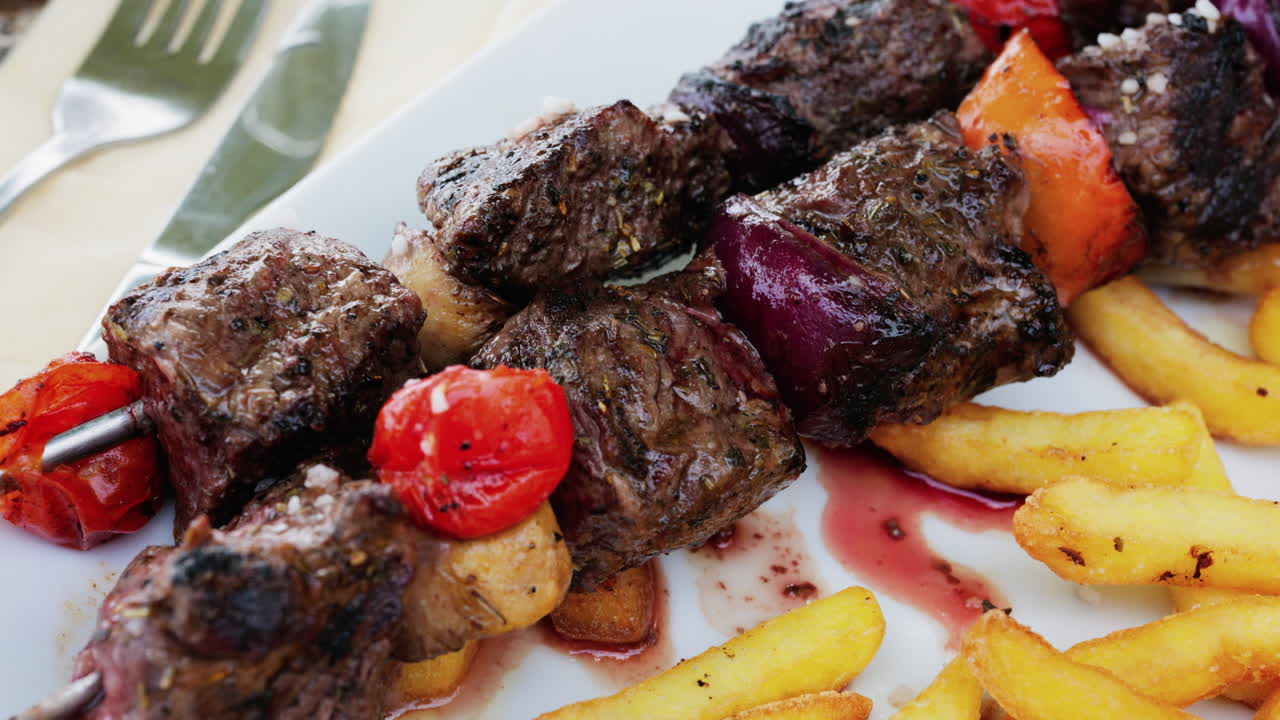Close up of grilled pork skewers with tomatoes and french fries in a white plate at a restaurant