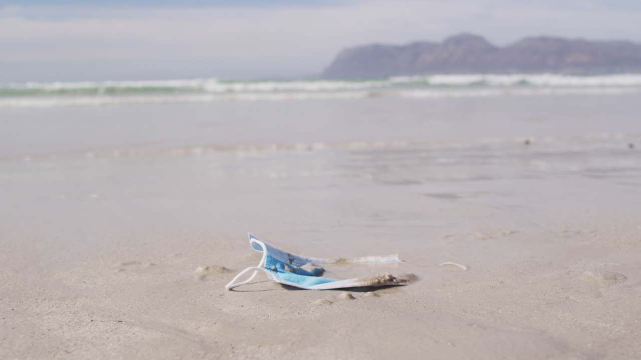 배경 에 파도 가 있는 해변 에 모래 에 누워 있는 얼굴 마스크