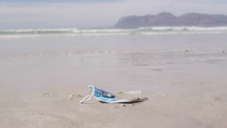 a face mask lying in sand on the beach with waves in the background