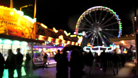 bokeh blur shot showing people walking over funfair during rainy day at night