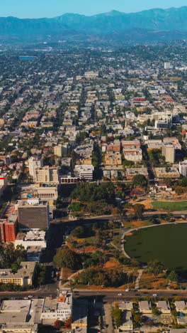 lovely park with a pond in the middle in the urban panorama. densely built los angeles cityscape at the backdrop of california mountains. vertical video