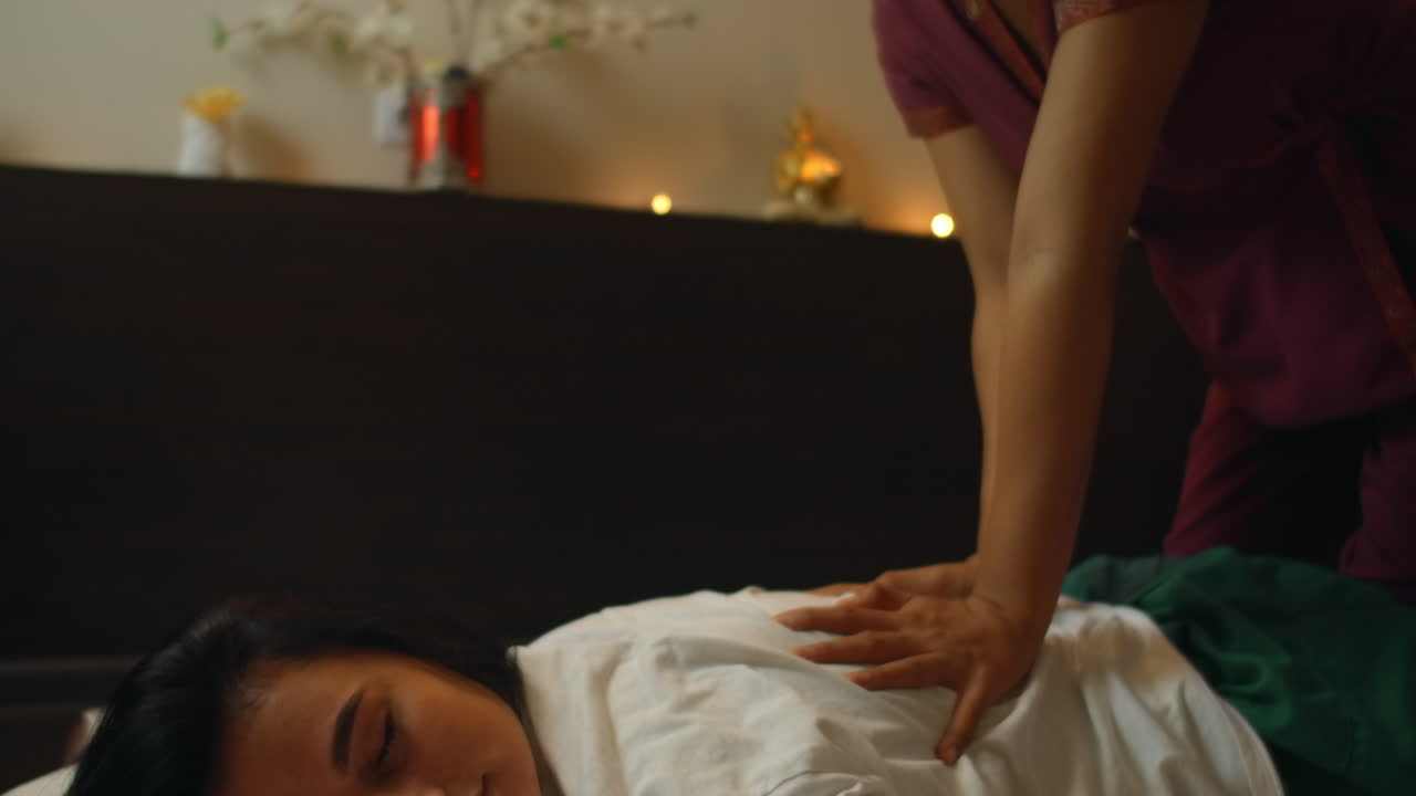 Asian Woman performs Traditional Thai Massage to beautiful European Woman. Rehabilitation and Treatment after Injuries with the help of Massage. Relax and Rest from massage of Legs Arms and Back. Therapeutic massage