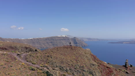 aerial: flying over one man standing at the top of hill in santorini, greece