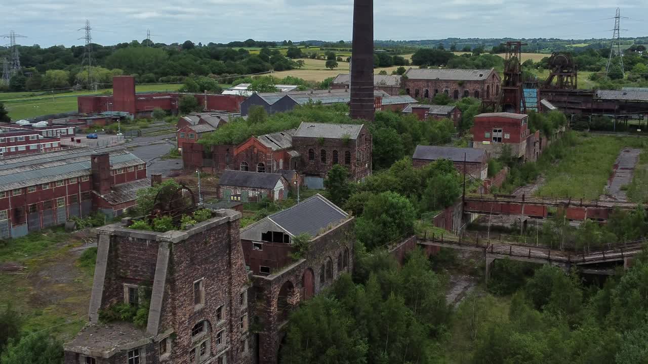 Luftfoto med zoom ind af forladte, gamle, tilgroede industrimuseumsbygninger ved en landlig kulmine.