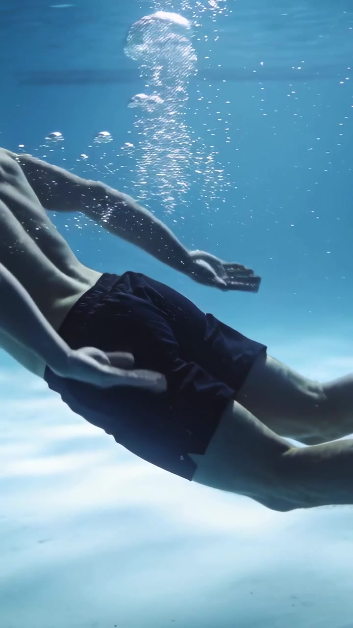 Video verticale: Uomo che scivola in pantaloncini da bagno neri mentre si allena in piscina, facendo bracciate ed espirando bolle.