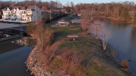 Imágenes-Aéreas-De-Drones-Volando-Desde-Un-Punto-De-Tierra-Sobre-Un-Lago-Con-Bonitas-Casas-Y-Muelles-Para-Barcos-Al-Atardecer