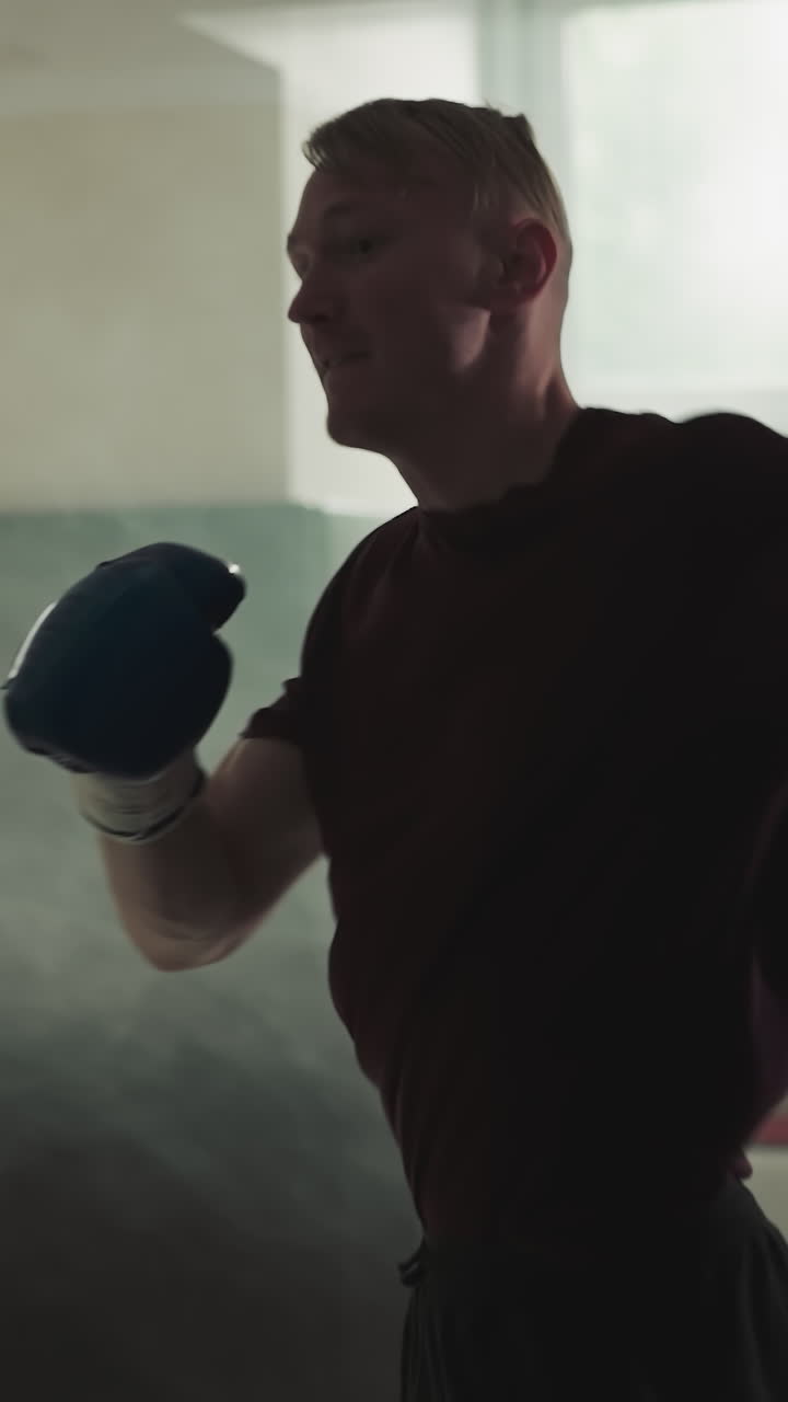 Sportsman exercises beating punching bag in sports center. Excited man punches equipment training in foggy gym slow motion. Martial arts champion