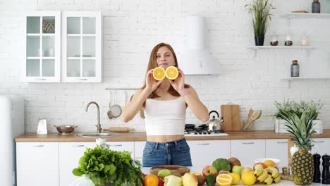 a young cheerful girl in the kitchen with fruits and vegetables is played with orange slices. the girl covers her eyes with slices of orange