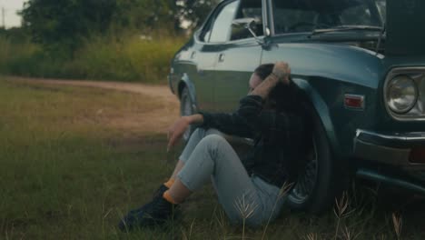 woman sitting beside broken down vintage car