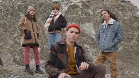 close up view of group of teenage friends dressed in winter clothes posing looking at camera, sitting and standing on the mountain