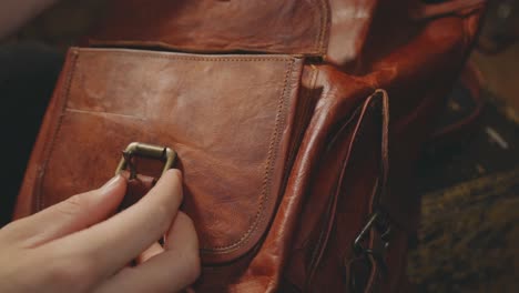 person's hand opening the leather bag belt buckle on the front