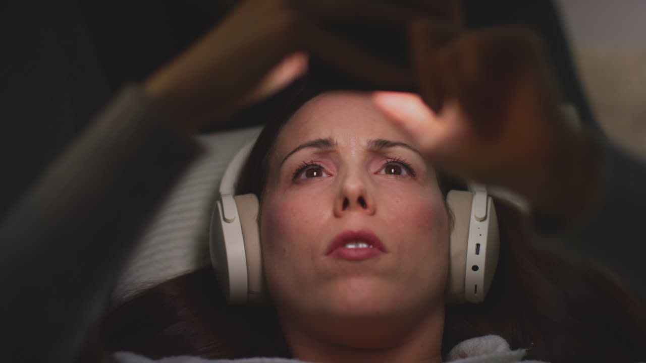 primer plano de una mujer con auriculares inalámbricos acostada en el sofá en casa por la noche transmitiendo o viendo contenido en línea en el teléfono móvil 1