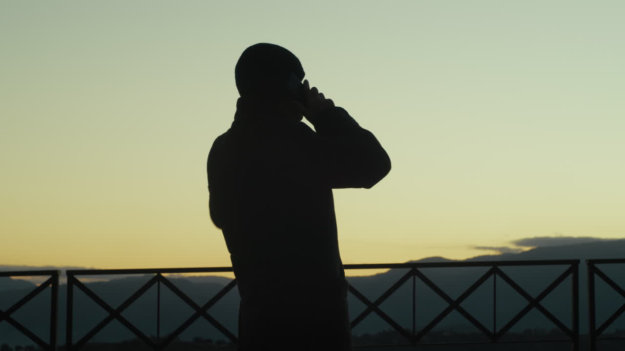 은이 남자가 드폰으로 이야기하고 해가 지는 동안 활기차게 몸짓을 하고 있다.