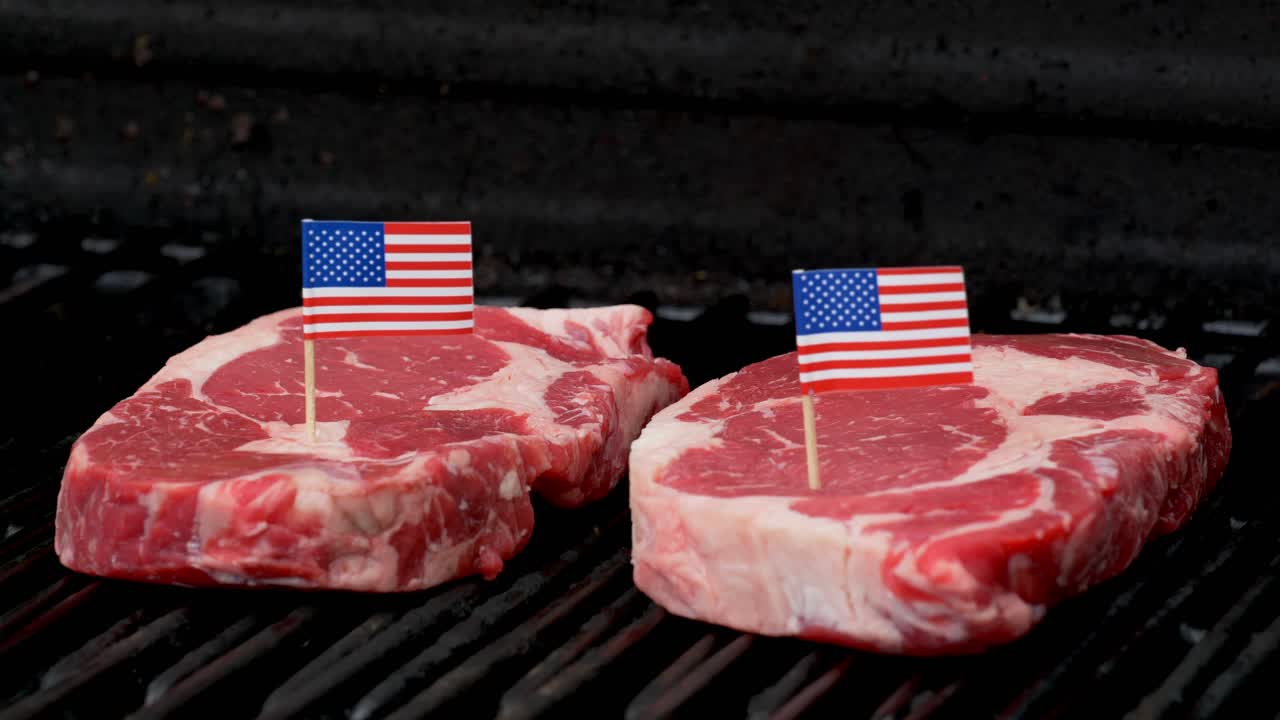 dos bistecs de rib-eye jugosos sentados en la parrilla y cocinados con dos diminutas banderas americanas metidas en ellos