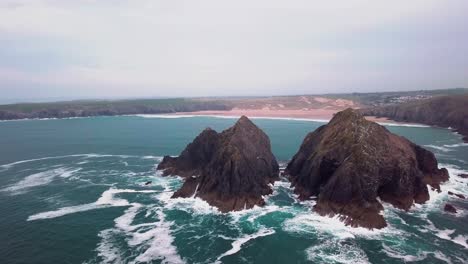 wide drone-shot of a rocky island in the foreground and the beach in the distance