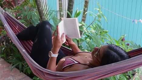 Hispanic-woman-swings-in-jungle-hammock,-reading-a-good-travel-book