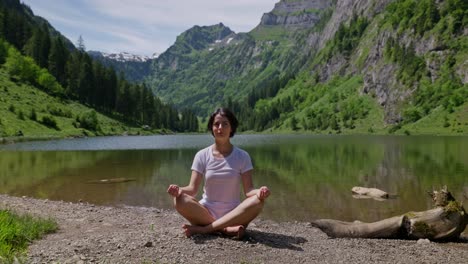 pretty woman practice yoga exercise on shore of lake between green mountains. sunny summer day in switzerland. snowy peak of mountains in background. close up.