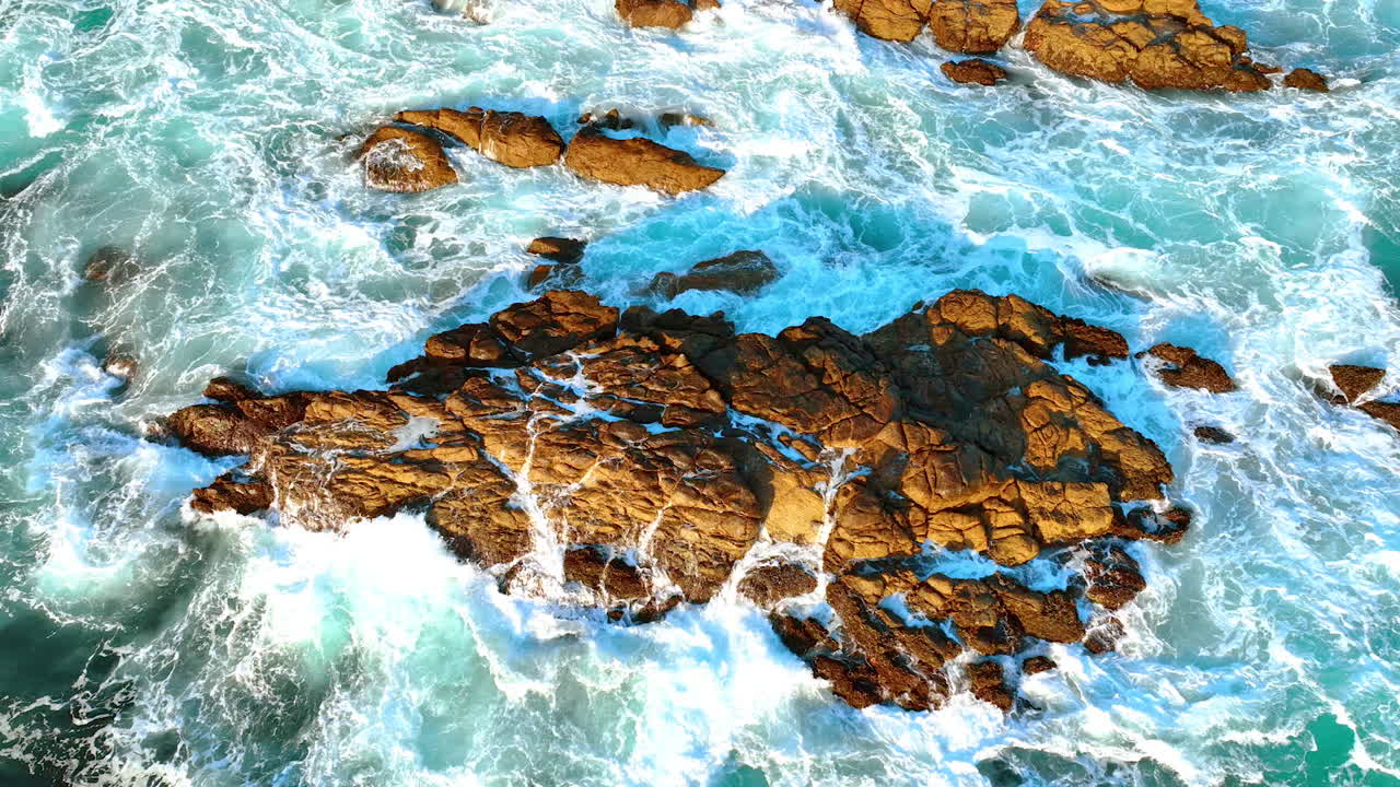 Bare rock sticking out of water. White foamy waves splash by the rock. Beautiful ocean at the shore. Top view.