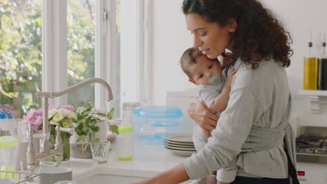 Madre-Feliz-Sosteniendo-A-Su-Bebé-Trabajando-En-Casa-Lavando-Platos-Limpiando-La-Cocina-Cuidando-A-Un-Niño-Pequeño-Haciendo-Tareas-Domésticas-Disfrutando-De-La-Maternidad