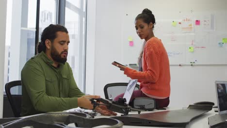 Mixed-race-male-and-female-business-colleagues-holding-drone-and-tablet-in-meeting-room