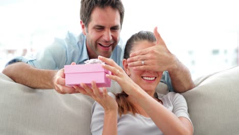 man surprising his girlfriend with a pink gift on the sofa