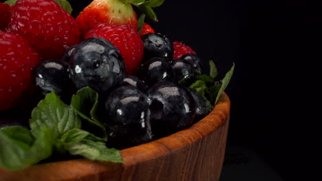 close up rotating forest berries in a wooden bowl with black background, strawberries, blueberries, raspberries, healthy fruits, 4k static shot