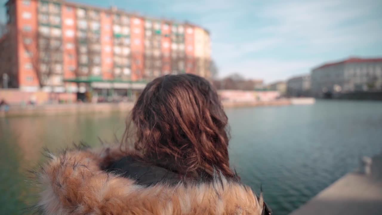 Young anonymous woman with curls walks along canal system Milan