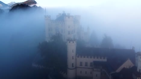 aerial view of hohenschwangau castle, bavaria, germany in morning autumn fog, revealing drone shot