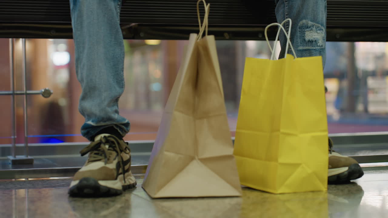 Close up of person in casual jeans and sneaker sitting with shopping bags on shiny mall floor reflecting light modern retail consumer lifestyle urban activity purchase