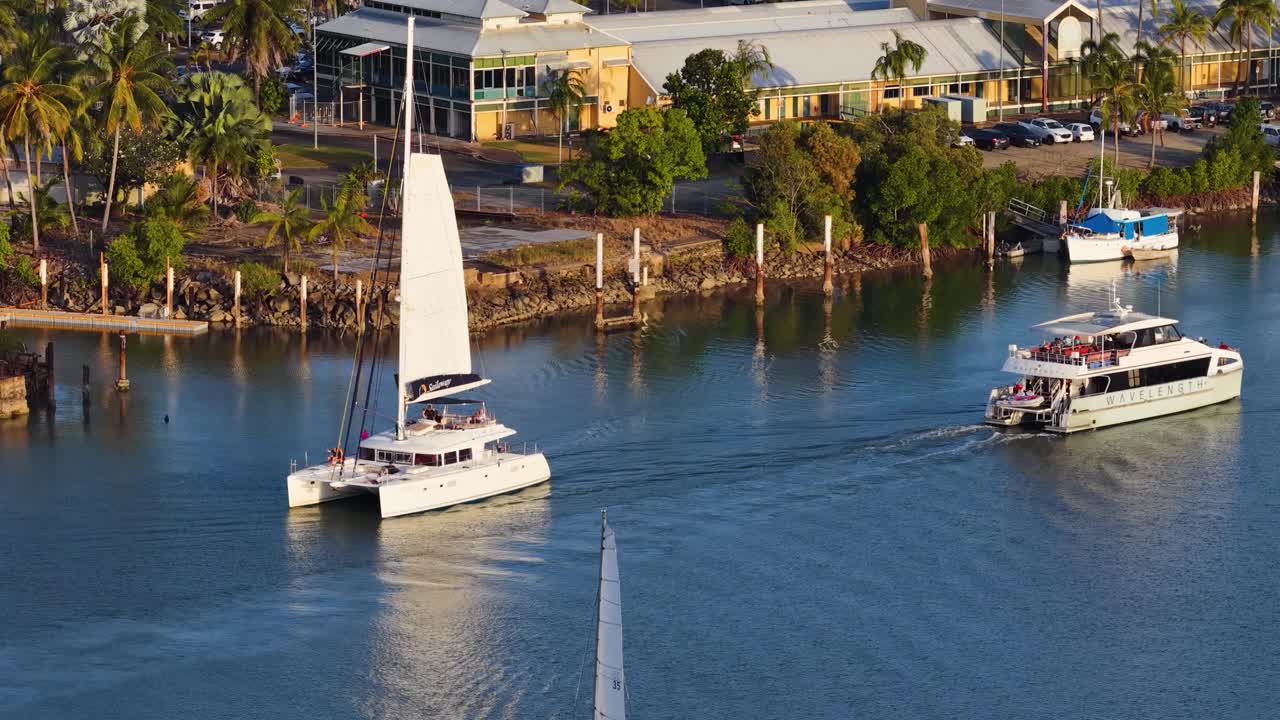 Drone footage captures boats navigating a tropical marina in Port Douglas, Australia, under clear skies and vibrant lighting