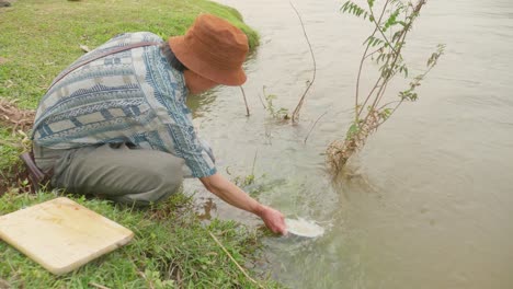 High-angle-shot-of-a-village-man-washing-his-porcelain-plates-in-river-water-in-loc-binh-in-a-rural-district-of-Lạng-Sơn-province-in-the-Northeast-region-of-Vietnam