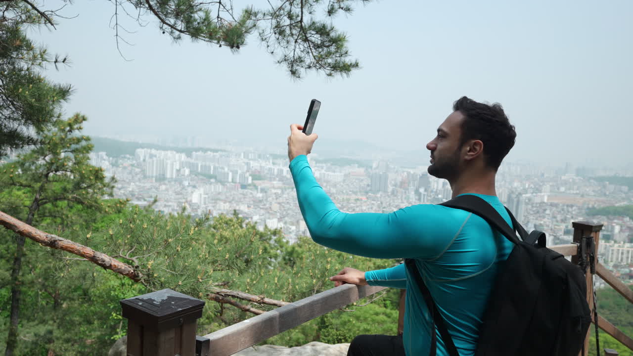 Man traveler taking pictures on mobile phone in Gwanaksan mountain, Seoul city in Background