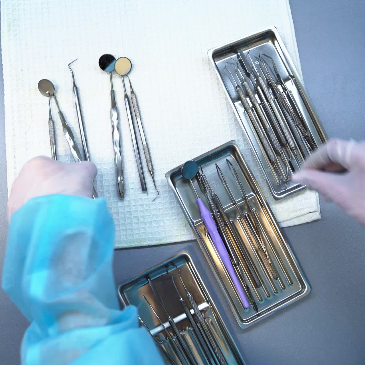 Preparation of metal tools for dental care check up. Nurse's gloved hands take the instruments from a table and divide them into several trays. Close up. Top view