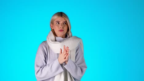 portrait of young blonde woman feeling cold, wearing scarf grey sweater and earmuffs, studio shot with pink background