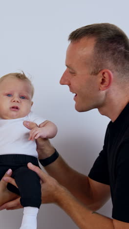tiny kid in hands of his parents. caucasian couple kissing their lovely baby on the cheeks. white backdrop. vertical video