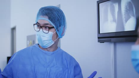 cirujano asiático con gorra quirúrgica y máscara facial discutiendo rayos x con colegas