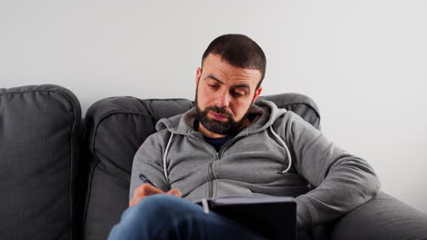 Man-Sitting-On-Sofa-And-Writing-In-His-Journal---Close-Up