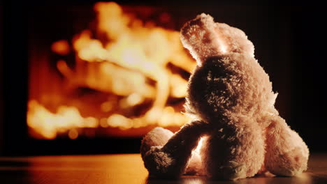 lonely plush rabbit admires the fire in the fireplace insert