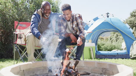 Glücklicher-Afroamerikanischer-Vater-Und-Sohn-Toasten-Marshmallows-über-Lagerfeuer,-Kopierraum,-Zeitlupe