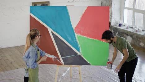 young couple in art studio together remove adhesive tape from their artwork