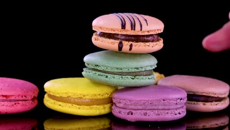 hand selects pastel macarons from glossy black surface, showcasing vibrant colors, texture, and arrangement