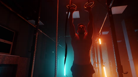 joven realiza pull-ups en anillos de gimnasia entrenamiento crossfit entrenamiento de día. ejercicio de gimnasia de lluvia usando anillos entrenamiento muscular intenso levantamiento de pesas. entrenamiento en cámara lenta en anillos de gimnasia