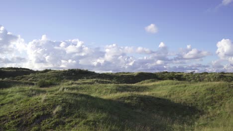 una toma amplia que se mueve cerca del suelo sobre una colina cubierta de hierba para revelar un paisaje de dunas en schiermonnikoog, waddenzee, países bajos