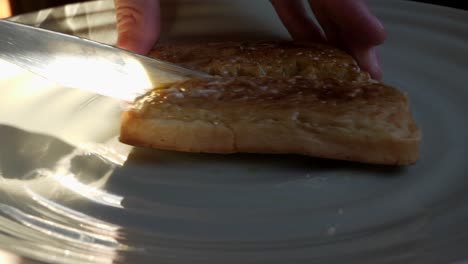 male hand cutting buttered crumpet in half on plate