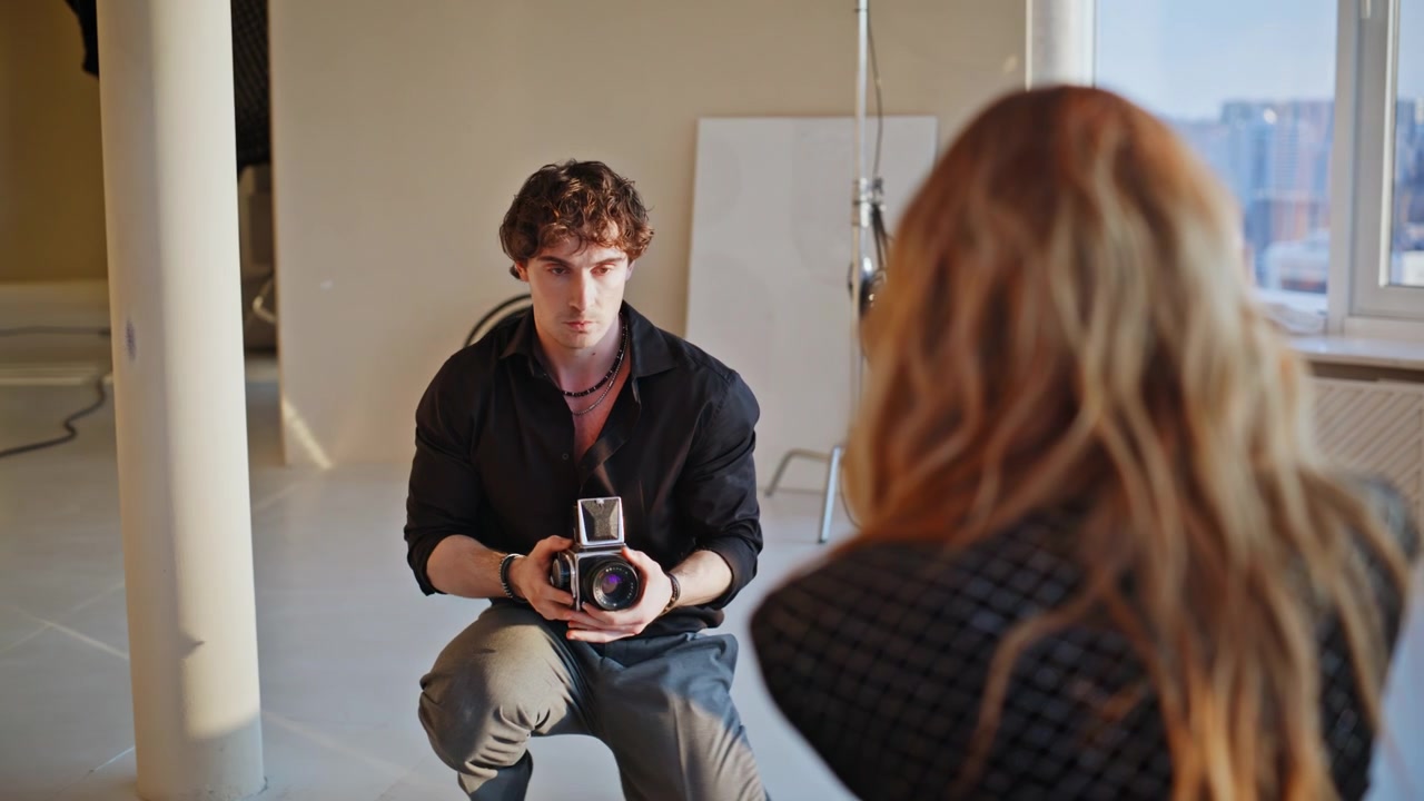 Fotografo con modella in uno studio per un servizio fotografico di moda. Uomo che tiene una macchina fotografica vintage