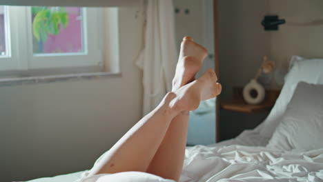 Closeup playful woman legs in bedroom sunlight. Happy girl dangling feet at home