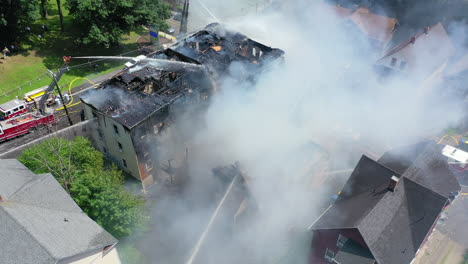 An-Apartment-Building-Smoulders-After-a-Fire-with-Firefighters-on-Scene,-Aerial-Rotating-Shot